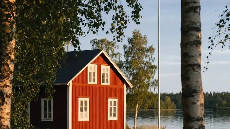 Puinen järvimökki rannassa, laituri ja tyyni vesi.
